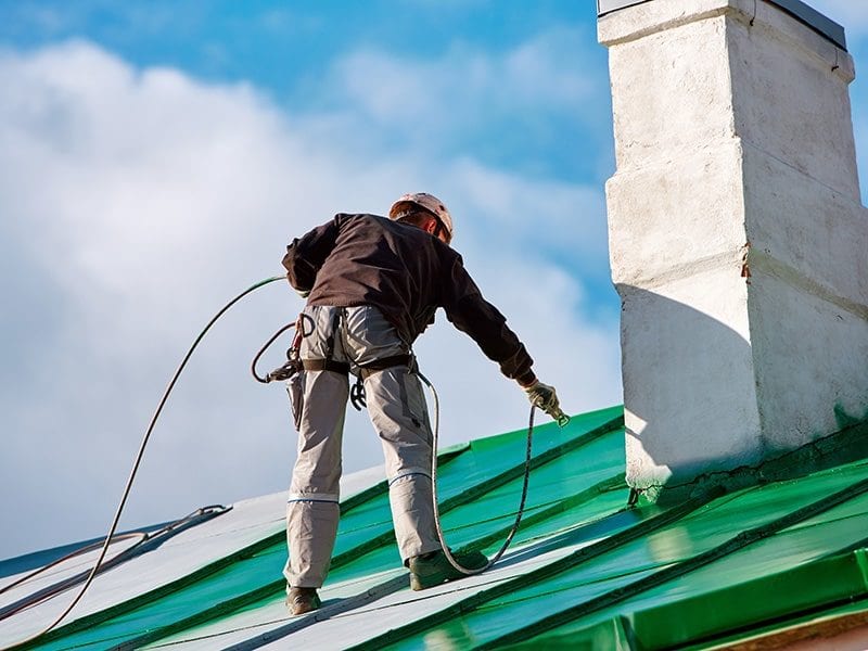 man on roof spraying heat reflective paint